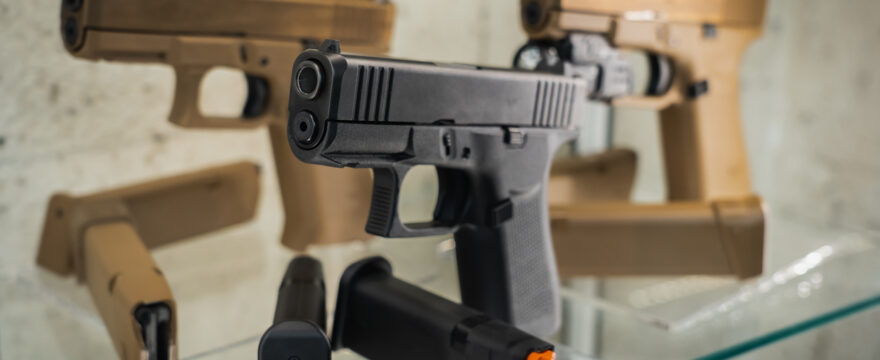 A black handgun and two brown handguns sit in a glass display case in a gun store.