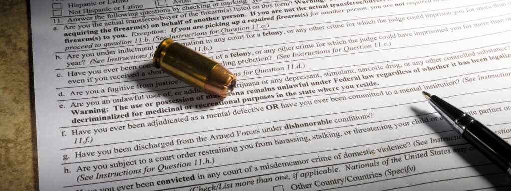 A handgun cartridge and a black pen sit on top of a firearm background check form.